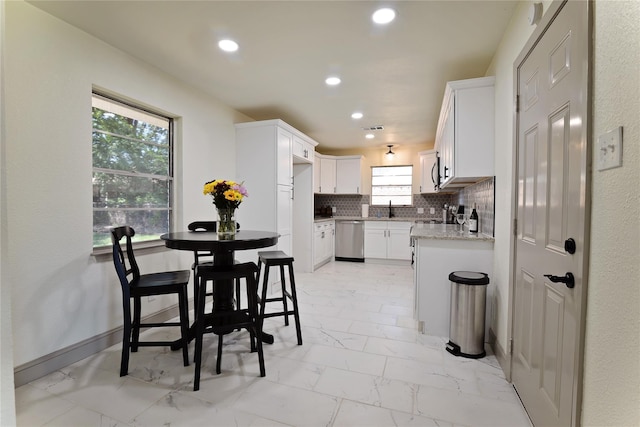 kitchen with white cabinetry, sink, backsplash, stainless steel dishwasher, and light stone counters