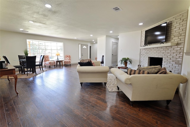 living room featuring dark hardwood / wood-style floors, a textured ceiling, and a brick fireplace