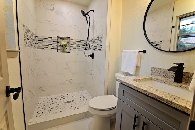 bathroom with a tile shower, vanity, and toilet