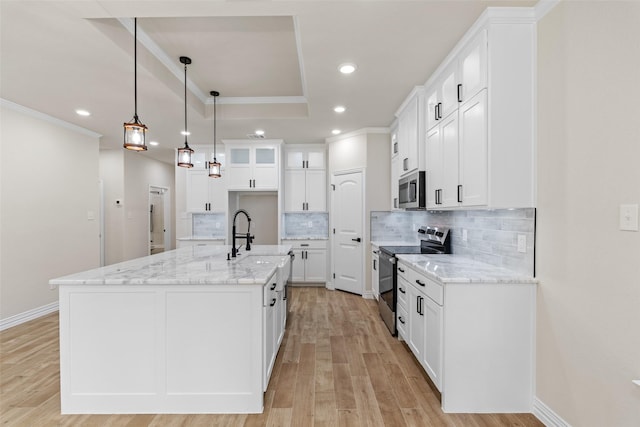 kitchen with white cabinets, appliances with stainless steel finishes, a center island with sink, and light hardwood / wood-style floors