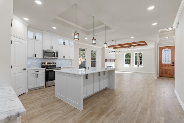 kitchen with stainless steel appliances, white cabinetry, a tray ceiling, and a healthy amount of sunlight