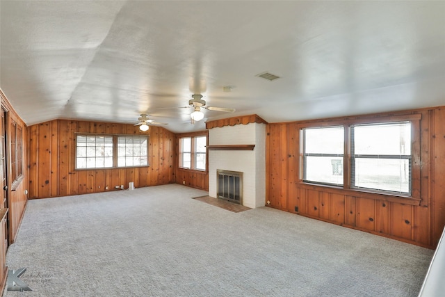 unfurnished living room featuring ceiling fan, a fireplace, vaulted ceiling, light colored carpet, and wood walls