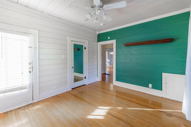 spare room with ornamental molding, hardwood / wood-style flooring, ceiling fan, and wooden walls