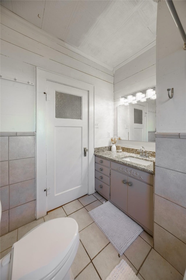 bathroom with tile patterned flooring, toilet, wooden walls, vanity, and tile walls