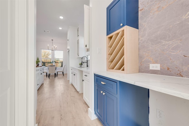 bar with sink, blue cabinetry, light stone countertops, white cabinets, and light wood-type flooring