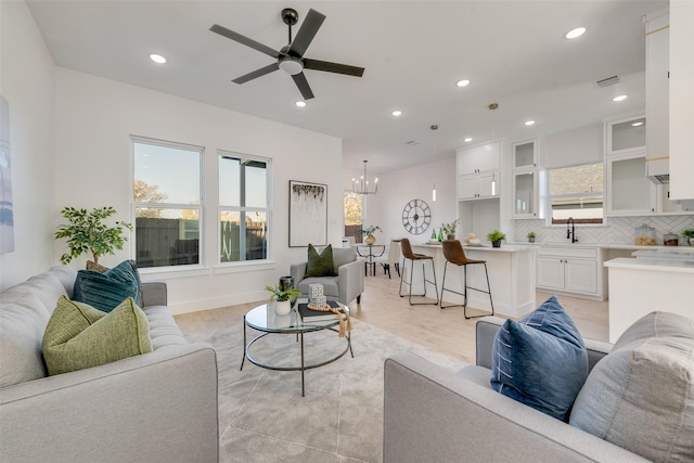 living room with sink, ceiling fan with notable chandelier, and light wood-type flooring