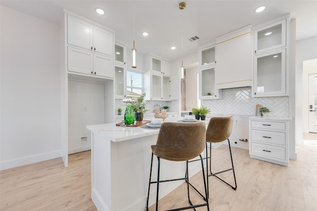 kitchen featuring white cabinets, hanging light fixtures, light wood-type flooring, tasteful backsplash, and a kitchen island