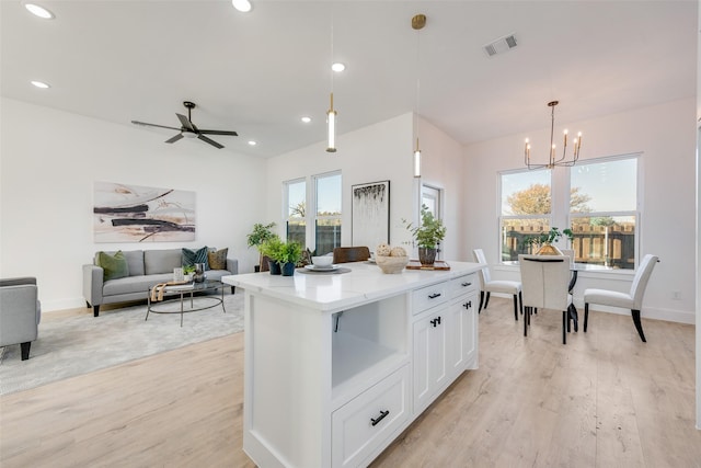 kitchen featuring white cabinets, ceiling fan with notable chandelier, hanging light fixtures, light hardwood / wood-style floors, and a kitchen island