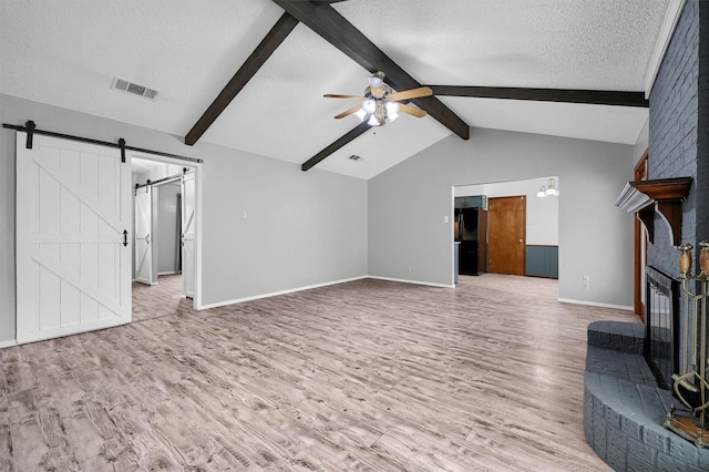 unfurnished living room with a fireplace, lofted ceiling with beams, wood-type flooring, a barn door, and a textured ceiling