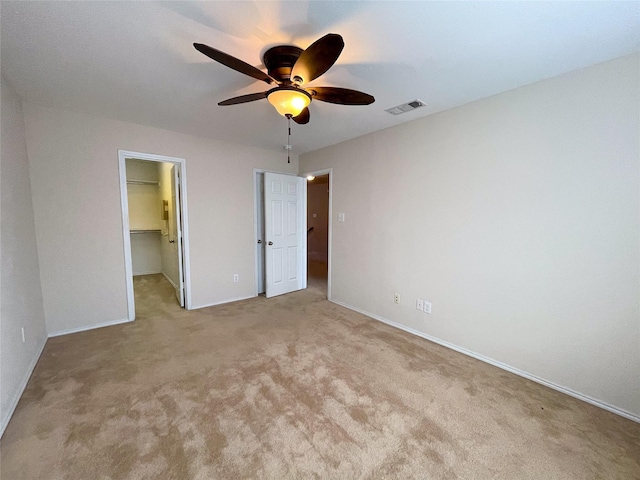 unfurnished bedroom with a spacious closet, light colored carpet, a closet, and ceiling fan