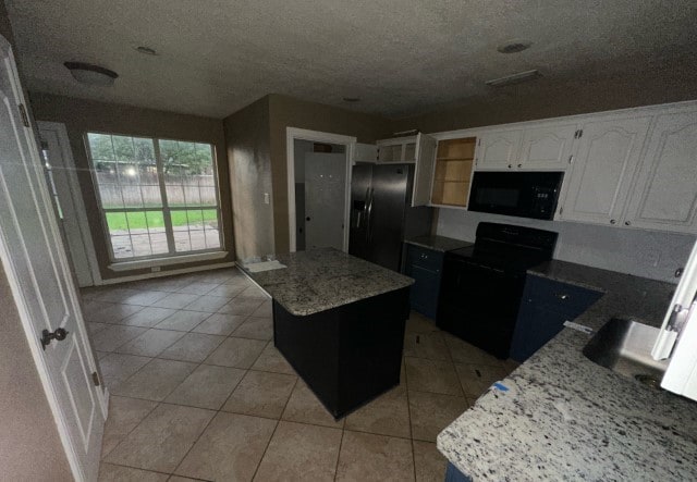 kitchen with light stone countertops, black appliances, white cabinets, a kitchen island, and light tile patterned flooring