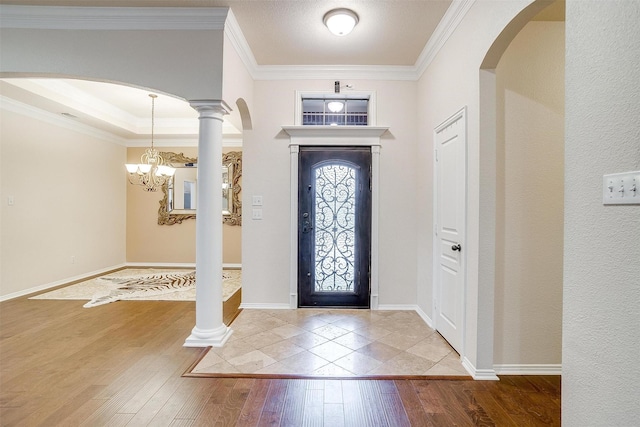 entrance foyer featuring hardwood / wood-style flooring, a notable chandelier, ornamental molding, and ornate columns