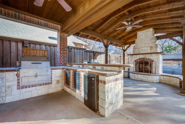 view of patio with an outdoor stone fireplace, sink, ceiling fan, and an outdoor kitchen