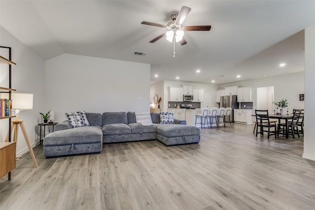 living room with light hardwood / wood-style floors, vaulted ceiling, and ceiling fan