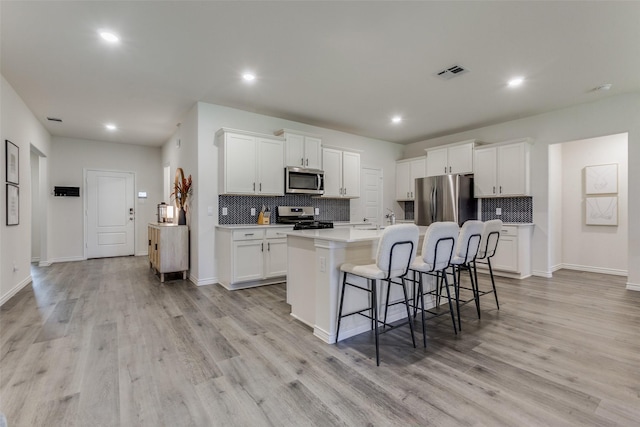 kitchen with a kitchen island with sink, white cabinetry, stainless steel appliances, and light wood-type flooring