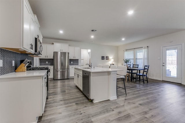 kitchen featuring appliances with stainless steel finishes, light wood-type flooring, a kitchen island with sink, sink, and white cabinetry