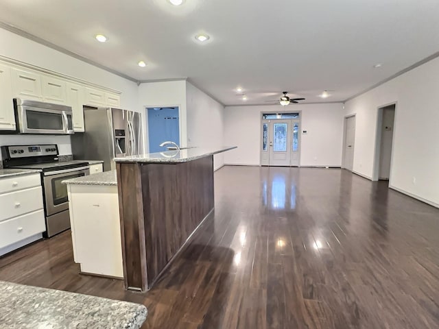 kitchen featuring dark wood-type flooring, appliances with stainless steel finishes, light stone countertops, and an island with sink