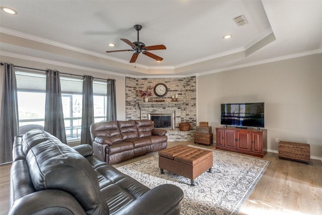 living room with light wood-type flooring, a tray ceiling, ceiling fan, and crown molding