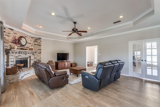 living room featuring a brick fireplace, light hardwood / wood-style floors, and a raised ceiling