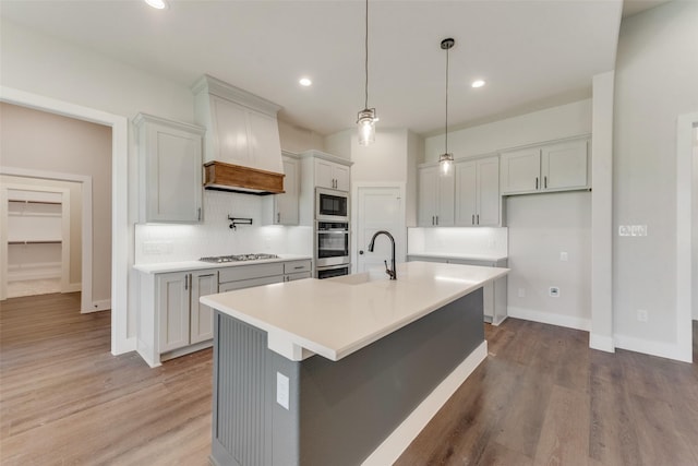 kitchen featuring hanging light fixtures, light hardwood / wood-style flooring, built in microwave, an island with sink, and tasteful backsplash