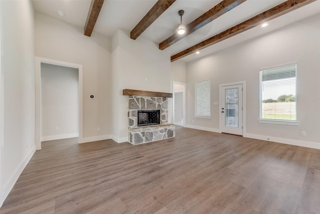 unfurnished living room featuring beamed ceiling, ceiling fan, light hardwood / wood-style floors, and a fireplace