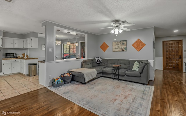 living room with crown molding, ceiling fan, light hardwood / wood-style flooring, and a textured ceiling