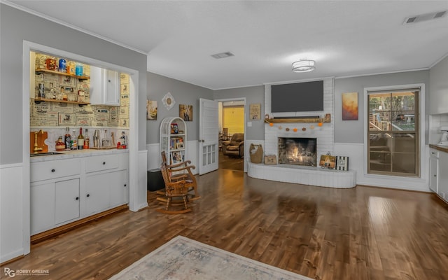 living room featuring ornamental molding, dark hardwood / wood-style flooring, and a brick fireplace