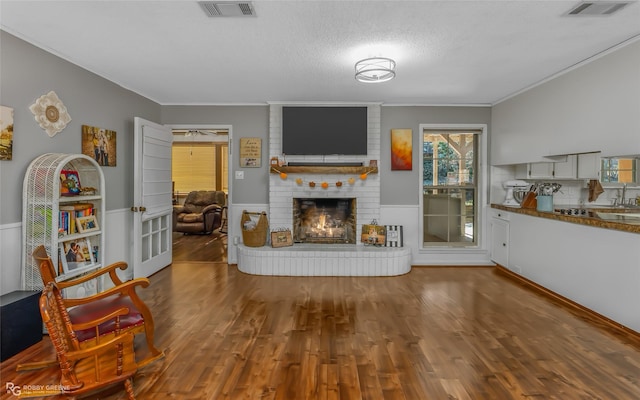 living room with wood-type flooring, a brick fireplace, a textured ceiling, and crown molding