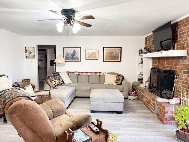 living area with light wood finished floors, a brick fireplace, and a ceiling fan