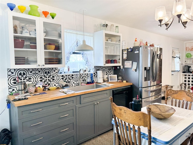 kitchen with butcher block counters, gray cabinetry, glass insert cabinets, a sink, and stainless steel fridge