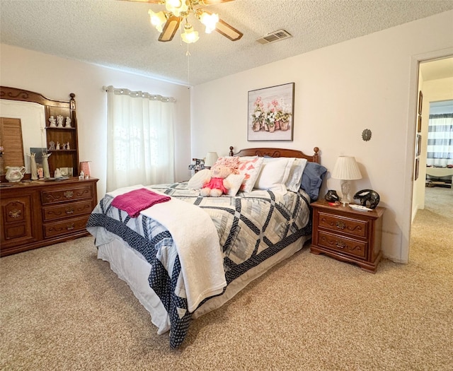 carpeted bedroom featuring a ceiling fan, visible vents, and a textured ceiling