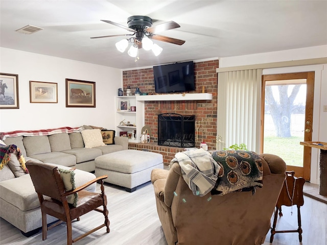 living area with ceiling fan, a brick fireplace, visible vents, and light wood-style floors