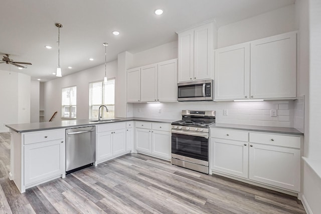 kitchen with sink, appliances with stainless steel finishes, kitchen peninsula, pendant lighting, and white cabinets