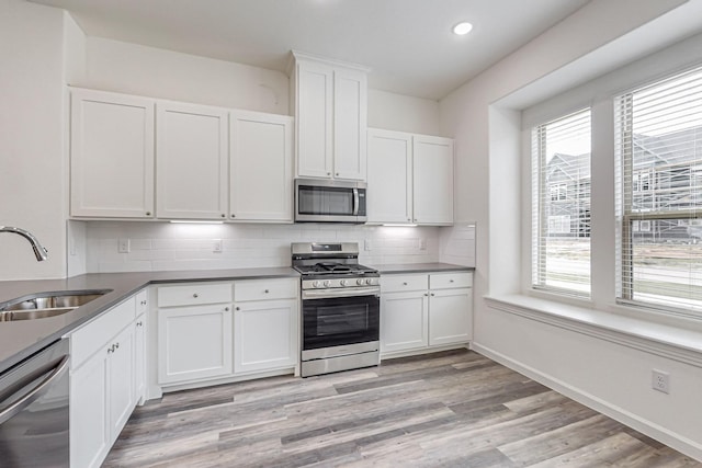 kitchen featuring appliances with stainless steel finishes, white cabinetry, sink, decorative backsplash, and light hardwood / wood-style flooring