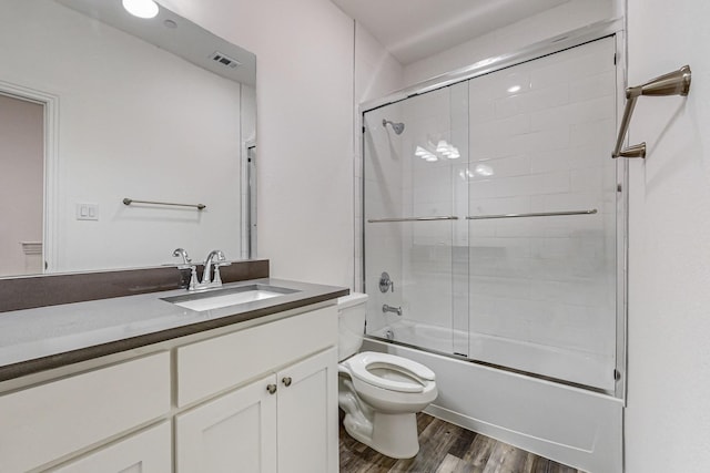 full bathroom featuring hardwood / wood-style flooring, bath / shower combo with glass door, vanity, and toilet