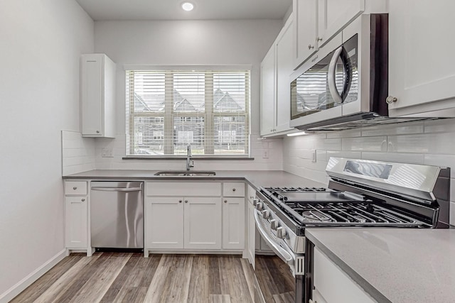 kitchen with sink, white cabinets, decorative backsplash, light hardwood / wood-style floors, and stainless steel appliances