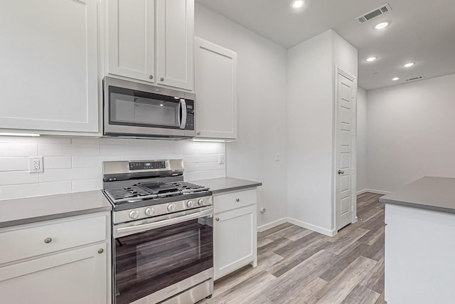 kitchen featuring decorative backsplash, light wood-type flooring, white cabinets, and appliances with stainless steel finishes