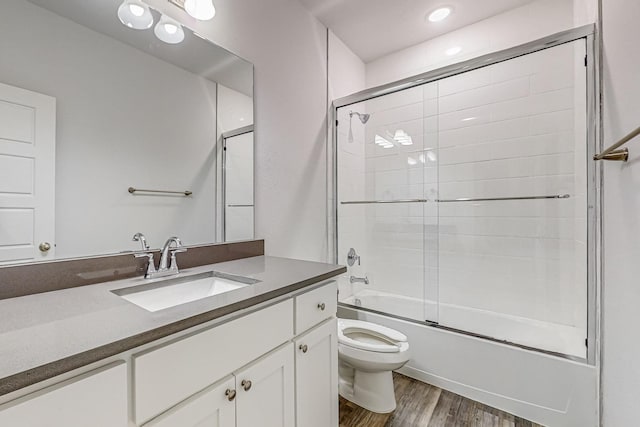 full bathroom with vanity, hardwood / wood-style flooring, shower / bath combination with glass door, and toilet