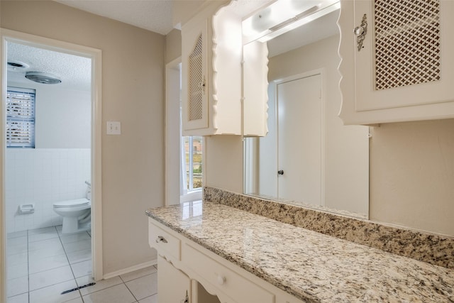 bathroom with tile patterned flooring, a textured ceiling, toilet, vanity, and tile walls