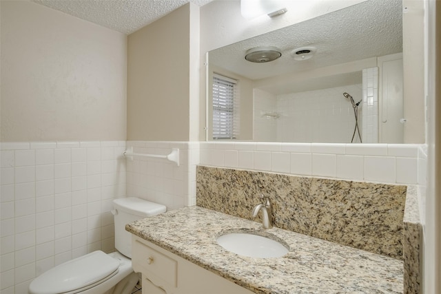 bathroom featuring a textured ceiling, vanity, tiled shower, tile walls, and toilet