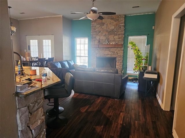 living room with dark hardwood / wood-style flooring, a stone fireplace, ceiling fan, and crown molding