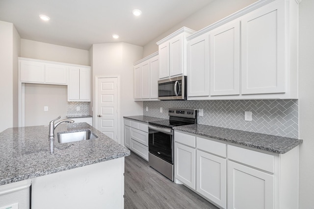 kitchen with appliances with stainless steel finishes, sink, dark stone countertops, white cabinets, and light hardwood / wood-style floors