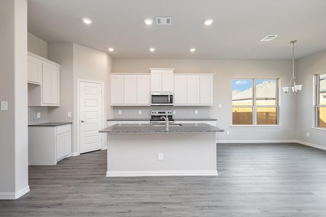 kitchen with dark hardwood / wood-style flooring, backsplash, a kitchen island with sink, white cabinets, and appliances with stainless steel finishes