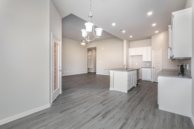 kitchen with decorative backsplash, wood-type flooring, a center island with sink, white cabinets, and hanging light fixtures