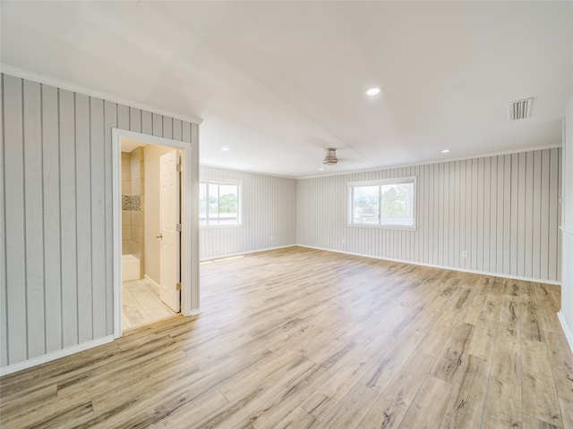 empty room with wooden walls, plenty of natural light, and light hardwood / wood-style floors