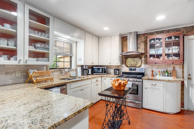 kitchen featuring light stone counters, stainless steel appliances, a sink, white cabinetry, and wall chimney exhaust hood