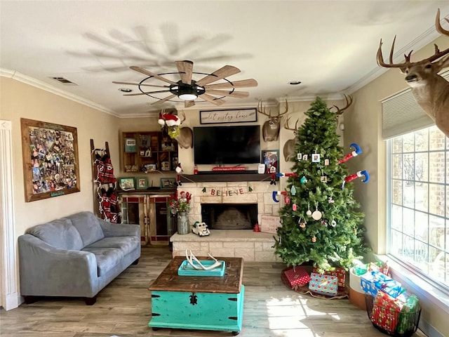 living room featuring hardwood / wood-style floors, ceiling fan, a stone fireplace, and crown molding