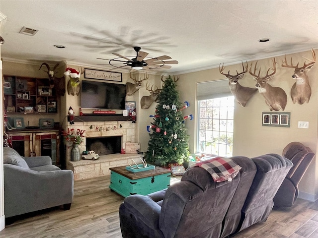 living room featuring a stone fireplace, ceiling fan, hardwood / wood-style floors, and crown molding