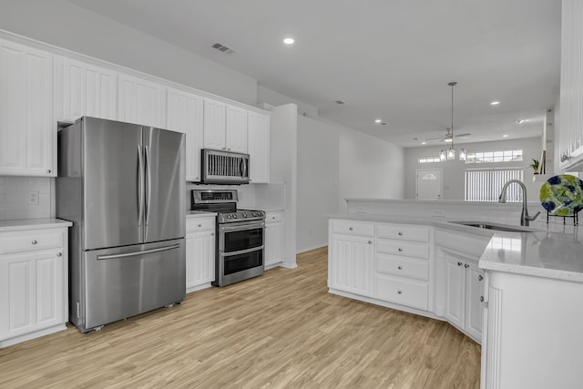 kitchen featuring decorative light fixtures, stainless steel appliances, visible vents, white cabinets, and a sink