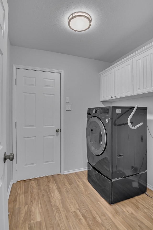 clothes washing area with a textured ceiling, baseboards, light wood-style floors, cabinet space, and washer / clothes dryer